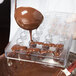A person using a Martellato ribbed oval chocolate mold to pour liquid chocolate.