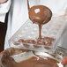 A person pouring chocolate into a Chocolate World polycarbonate mold.