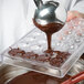 A person pouring liquid chocolate into a Matfer Bourgeat half circle chocolate mold.