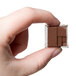 A hand holding a square Chocolate World chocolate cube.