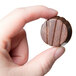 A hand holding a Matfer Bourgeat chocolate candy with striped circles.