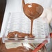 A person pouring liquid chocolate into a Matfer Bourgeat plastic tray with tulip rectangle molds.