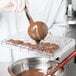 A person using a spoon to pour chocolate into a Matfer Bourgeat chocolate mold.