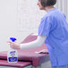 A woman in blue scrubs using Purell Fragrance Free Healthcare Surface Disinfectant to clean a surface.