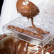 A person using the Chocolat Form Polycarbonate Bullion Chocolate Mold to pour chocolate into a tray.