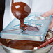 Liquid chocolate being poured into a Matfer Bourgeat clear plastic container.