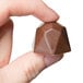 A hand holding a diamond-shaped chocolate candy.
