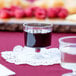 A clear plastic pedestal wine cup filled with red liquid on a doily on a table.