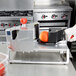 A gloved hand uses a Vollrath Redco InstaSlice fruit and vegetable cutter to slice an orange.