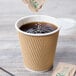 A close-up of a Lavex Kraft paper hot cup of coffee with a bag of sugar on the table.