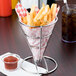 A Clipper Mill stainless steel wire cone basket filled with french fries and a drink.