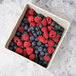 A square GET deli crock filled with blueberries and raspberries on a table.