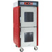 A red and silver Metro hot holding cabinet with clear Dutch doors and wheels.