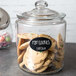 A glass jar of cookies with a black oval chalkboard label on a counter.