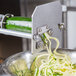 A Nemco Noodler front plate assembly on a Nemco zucchini noodle machine being used.