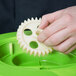 A hand holding a green plastic gear with a white background.