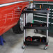 A black Luxor tool cart with tools on it next to a red car.