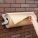 A person using a Bulman paper dispenser to cut brown paper on a brick wall.