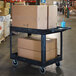 A Luxor black heavy-duty utility cart with two tub shelves full of boxes.