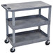 A Luxor gray plastic utility cart with two tub shelves and one flat shelf and wheels.