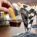 A hand dipping a french fry into sauce in a Clipper Mill mini metal cone basket.