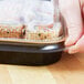 A hand placing a Durable Packaging mini foil entree container with black and gold lid on a counter.