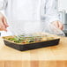 A chef holding a Durable Packaging black and gold aluminum foil tray with clear dome lid full of food.