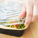 A hand placing a plastic lid on a Durable Packaging black and gold aluminum foil pan filled with salad.