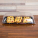 A Sabert black plastic catering tray with three muffins on it on a table in a bakery display.
