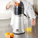 A person uses the AvaMix splash guard to juice oranges in a juicer.