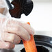 A gloved hand using the AvaMix pusher to peel a carrot.
