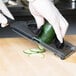 A person using a Mercer Culinary dual thickness hand slicer to slice a cucumber.