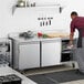 A man in a professional kitchen using an Avantco worktop refrigerator.