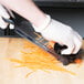 A person in gloves using a Mercer Culinary Julienne Hand Slicer to cut carrots on a cutting board.