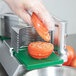 A tomato being sliced with a Garde 3/16" tomato slicer on a counter.