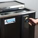 A hand opening a brown bottle of beer into an Avantco horizontal bottle cooler.