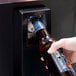 A hand opening a bottle of beer with a key using an Avantco bottle cooler.