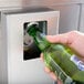 A hand opening a bottle of beer with an Avantco bottle cooler.
