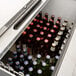 An Avantco stainless steel horizontal bottle cooler on a counter full of beer bottles.