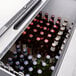 An Avantco black horizontal bottle cooler on a bar counter full of beer bottles.