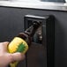A hand inserting a beer bottle into an Avantco Black Horizontal Bottle Cooler.