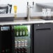 An Avantco black double tap kegerator with beer bottles and a tap.