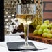 A Fineline clear plastic wine goblet filled with white wine sitting on a table next to grapes.
