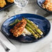 A GET Cosmo blue melamine plate with asparagus and chicken on a table.