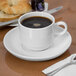 A Libbey white porcelain soup cup on a saucer with a croissant and jam next to a cup of coffee.