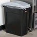 A black Rubbermaid Slim Jim trash can with a light gray handled lid and a plastic bag over it.