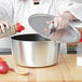 A woman pouring sauce from a spoon into a Vollrath Tapered Non-Stick Aluminum Sauce Pan with a black silicone handle.