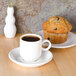 A cup of coffee on an Arcoroc porcelain saucer with a muffin on a plate.