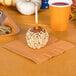 A Creative Converting pumpkin spice orange luncheon napkin with a caramel apple and a cup of drink on a table.