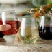 A hand holding a Visions plastic stemless wine sampler glass full of red wine.
